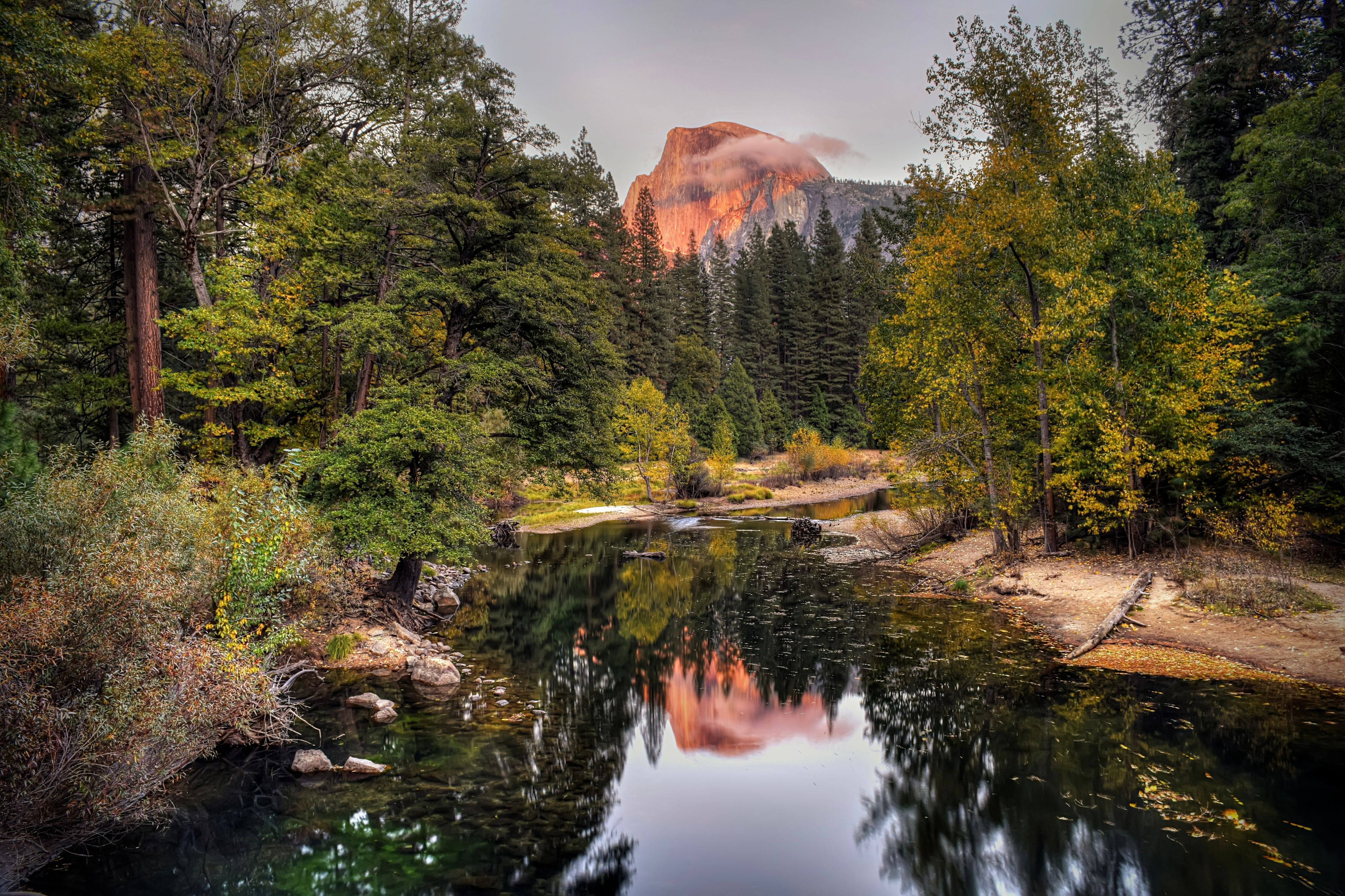 A serene river reflecting trees and a mountain.