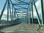 A bridge with a metal truss structure and a road with yellow lines.