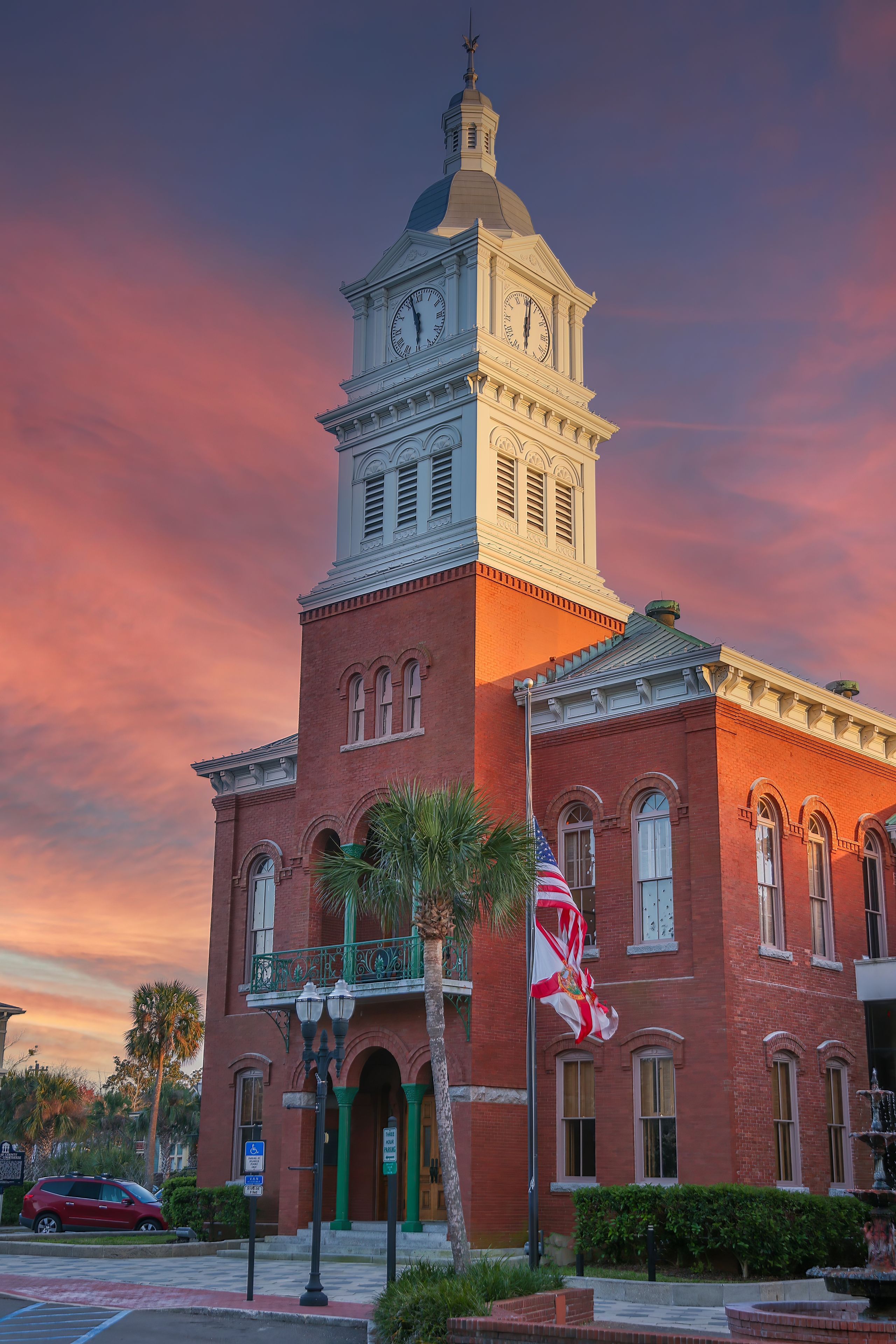 A historic building with a clock tower, red brick facade, and a flagpole with the American flag.