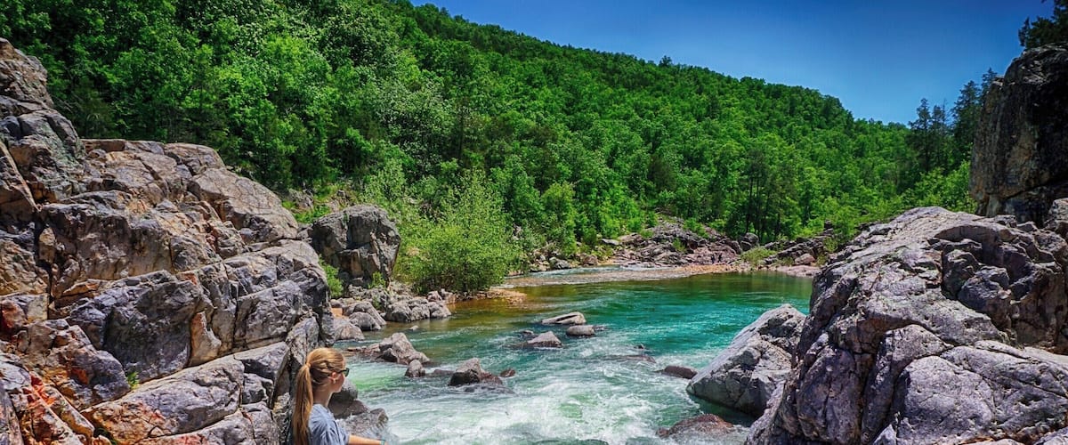 A river flowing through a rocky landscape with dense green forest in the background.