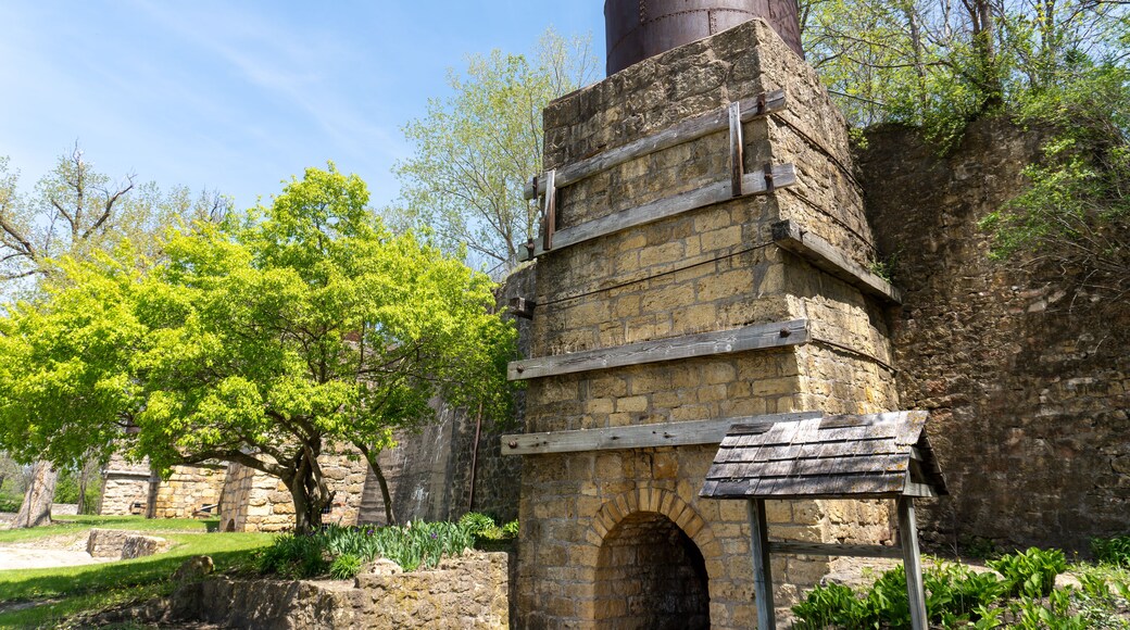 A historical stone structure with a cylindrical chimney, surrounded by greenery and trees.