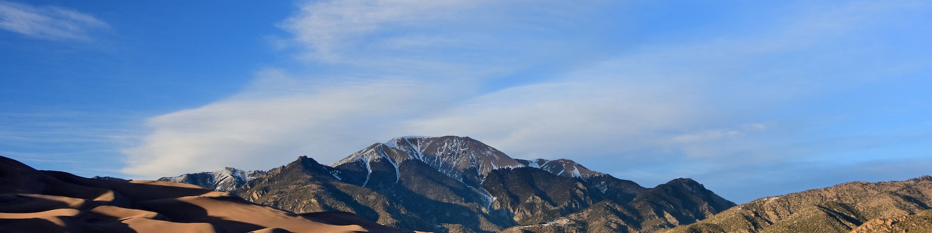 A desert landscape with sand dunes and snow-capped mountains under a clear sky.