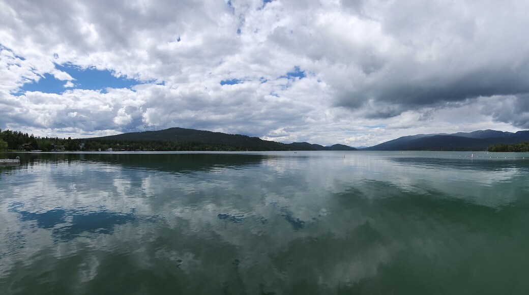 Whitefish Lake in Flathead County, Montana under dramatic summer cloudscape reflected in calm water of lake.