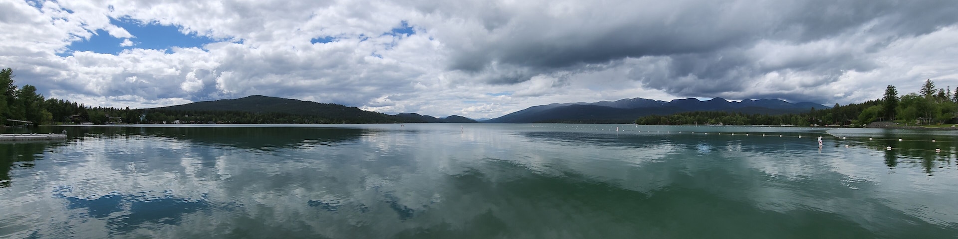 Whitefish Lake in Flathead County, Montana under dramatic summer cloudscape reflected in calm water of lake.
