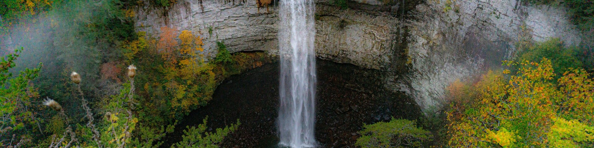 Falls Creek Falls is surrounded by vibrant fall colors and a misty morning haze. The waterfall cascades from a rocky cliff into a dark pool below. Photographed at Falls Creek Falls State Park in TN