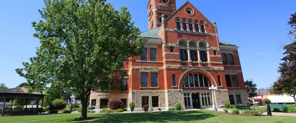 A large brick building with a clock tower and a green lawn in front.