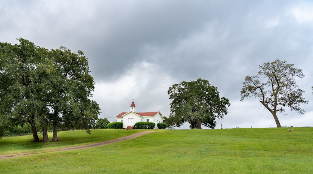 A white church with a red roof on a grassy hill under a cloudy sky.
