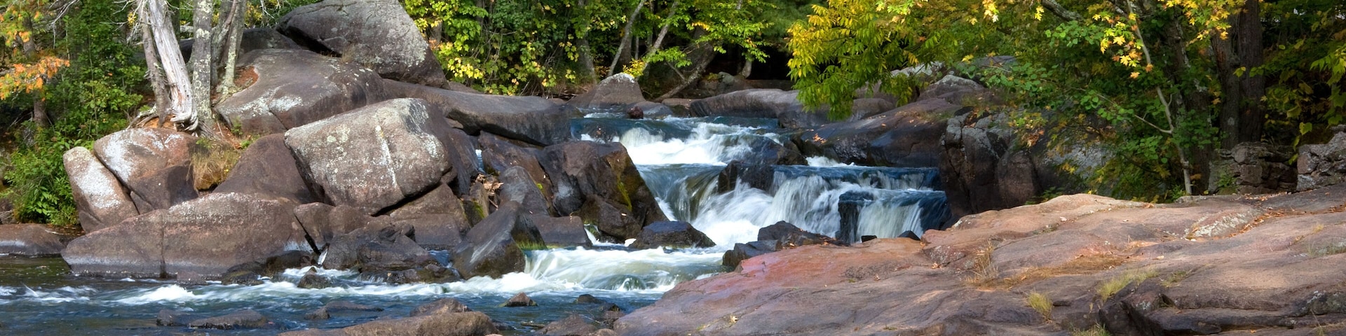 A river flowing over rocks with autumn foliage in the background.
