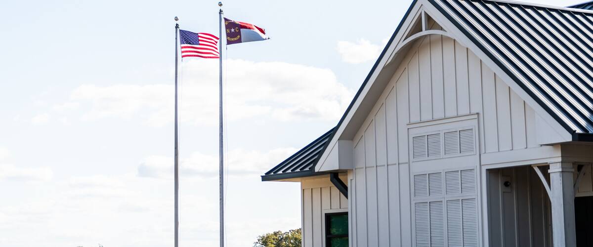 A white building with a sloped roof and a flagpole with two flags, one of which is the American flag.
