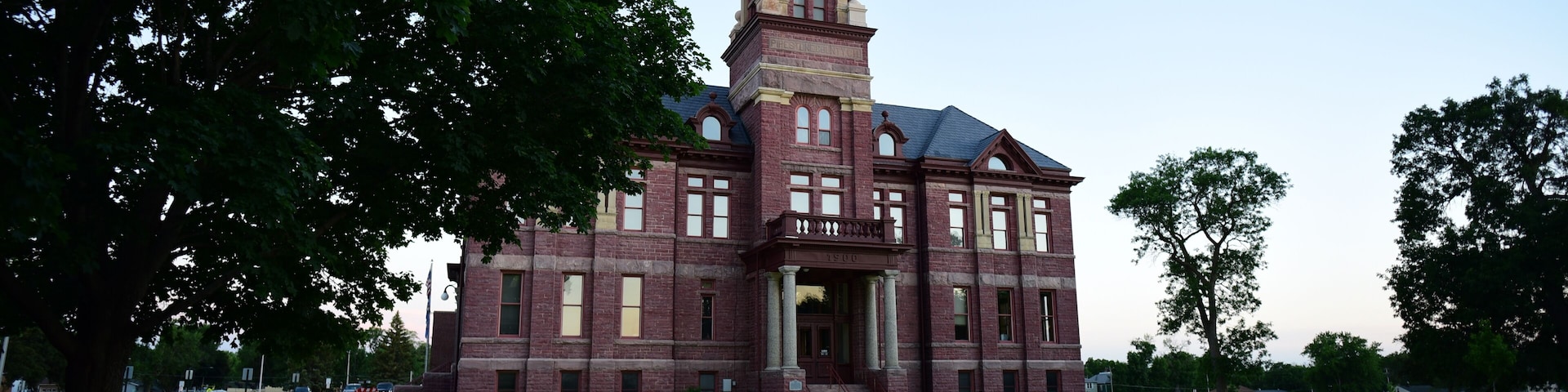 A large brick building with a clock tower and a lawn in front.