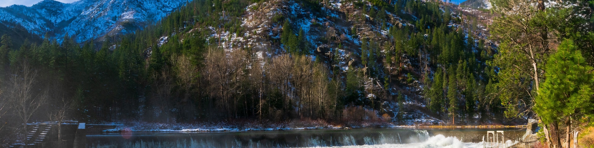 Un río con cascada, rodeado de montañas nevadas y árboles.
