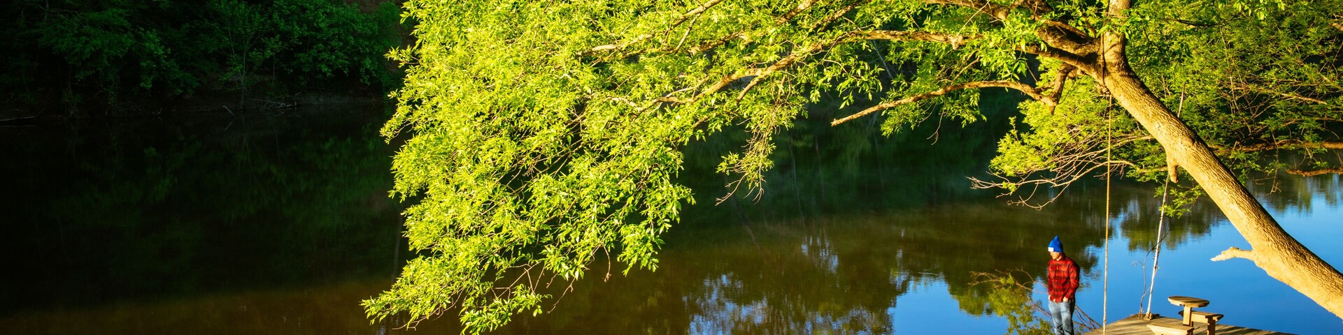 A man in a red jacket stands on a boat dock in the sun along the cape fear river in north carolina