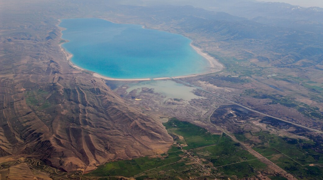 A large body of water surrounded by mountainous terrain and agricultural fields.