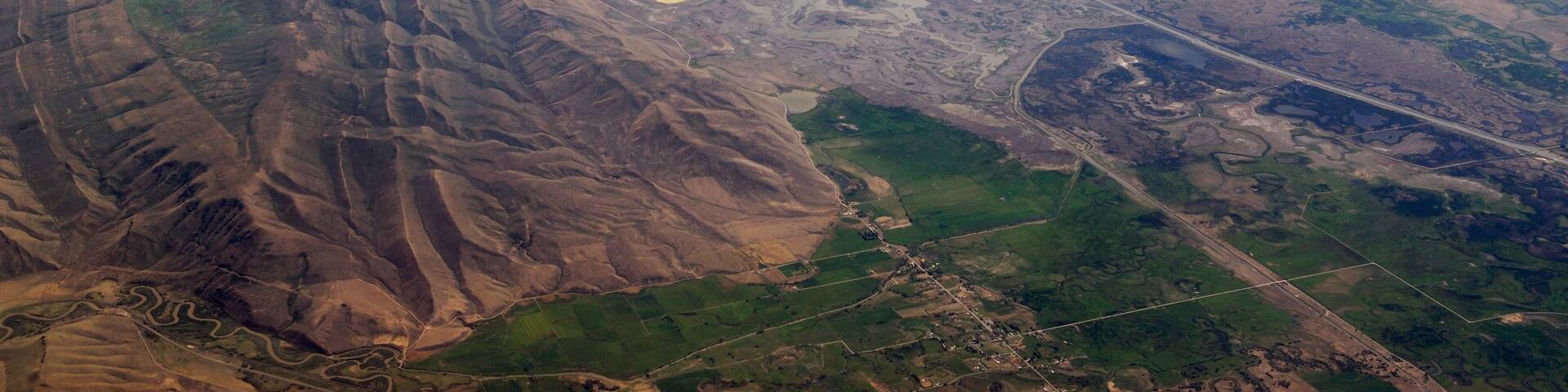 A large body of water surrounded by mountainous terrain and agricultural fields.