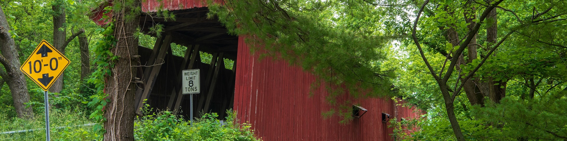 A red covered bridge with a 'Weight Limit 8 Tons' sign and a '10'-0" clearance' warning sign.