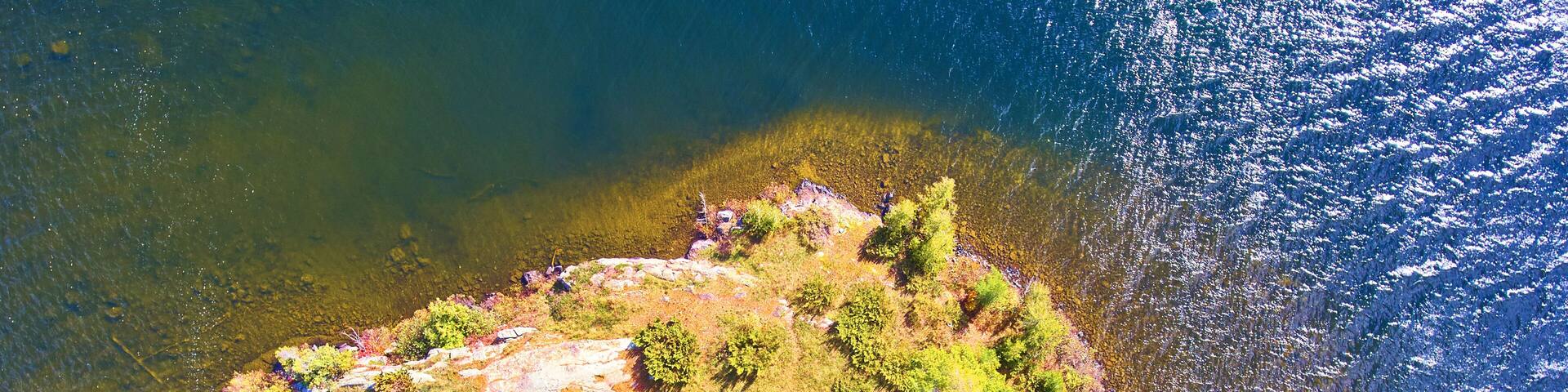 An aerial view of a small island with dense green vegetation and rocky outcrops surrounded by clear water.