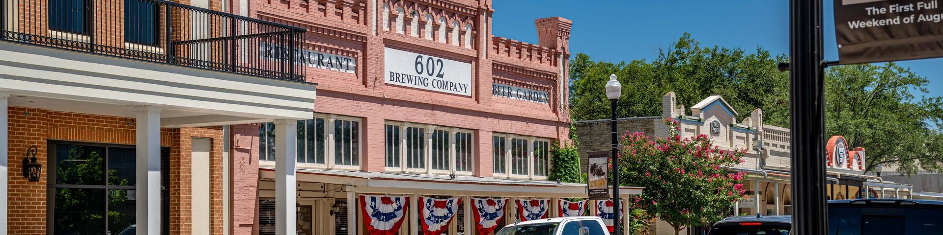 A street with a brick building labeled '602 BREWING COMPANY,' a white pickup truck, and a silver car.