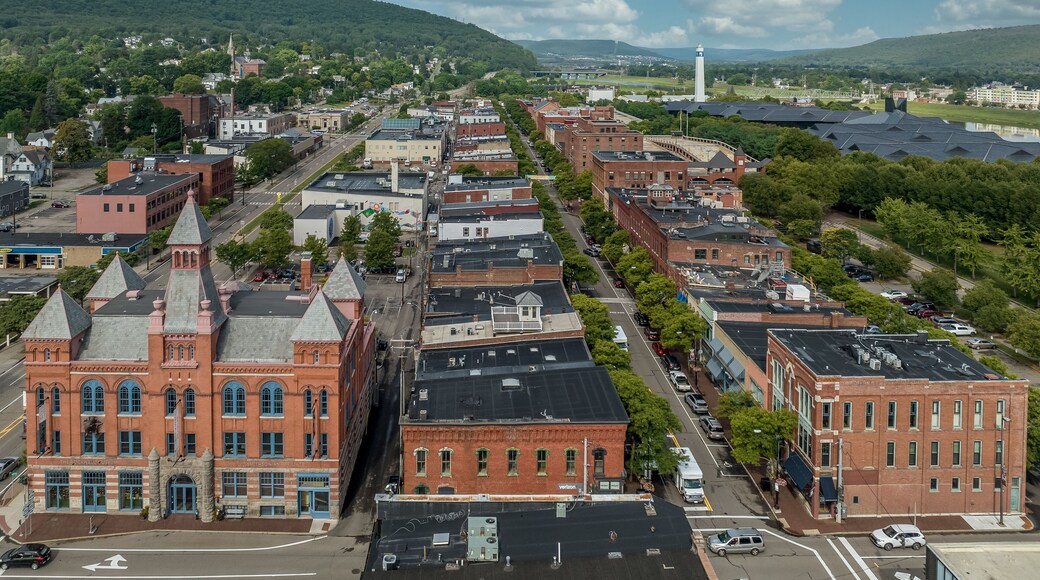 Aerial view of Corning Steuben County, New York downtown, Market Street, glass factory, chemung river, centerway walking bridge, little joe tower, parking lot with cloudy blue sky
