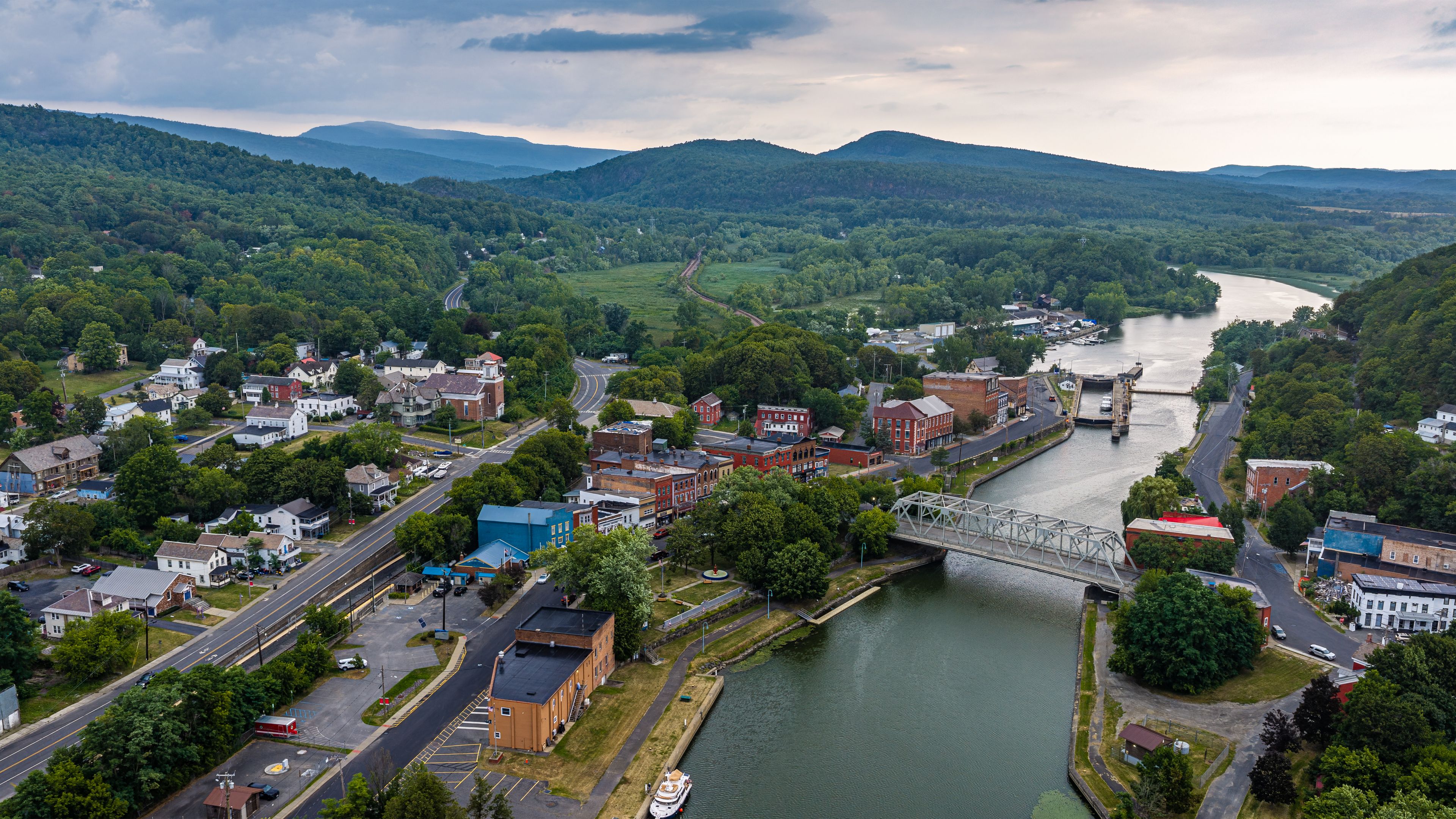 A river flowing through a town with a bridge, surrounded by hills and greenery.