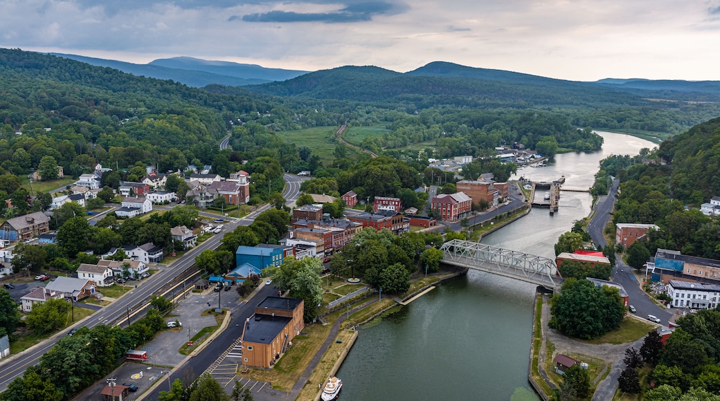 A river flowing through a town with a bridge, surrounded by hills and greenery.