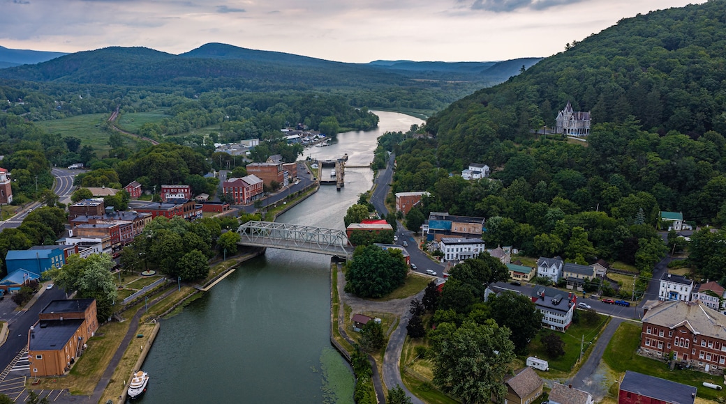 A river flowing through a town with a bridge, surrounded by hills and greenery.
