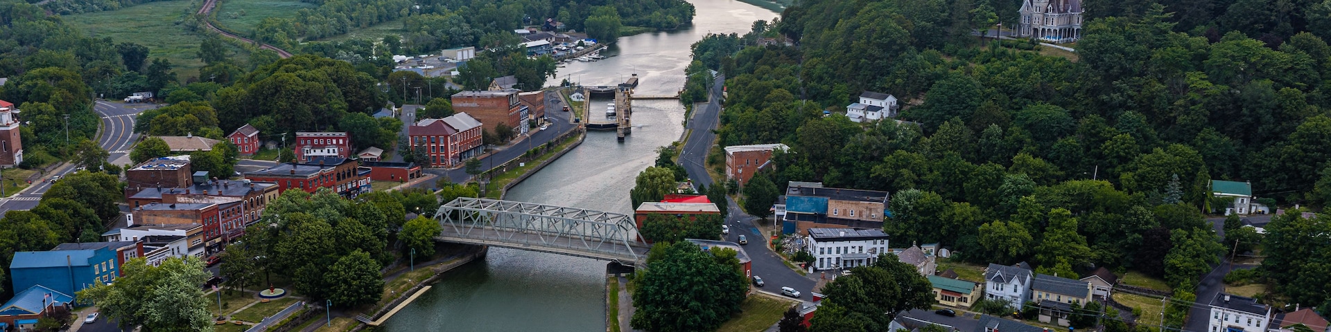 A river flowing through a town with a bridge, surrounded by hills and greenery.