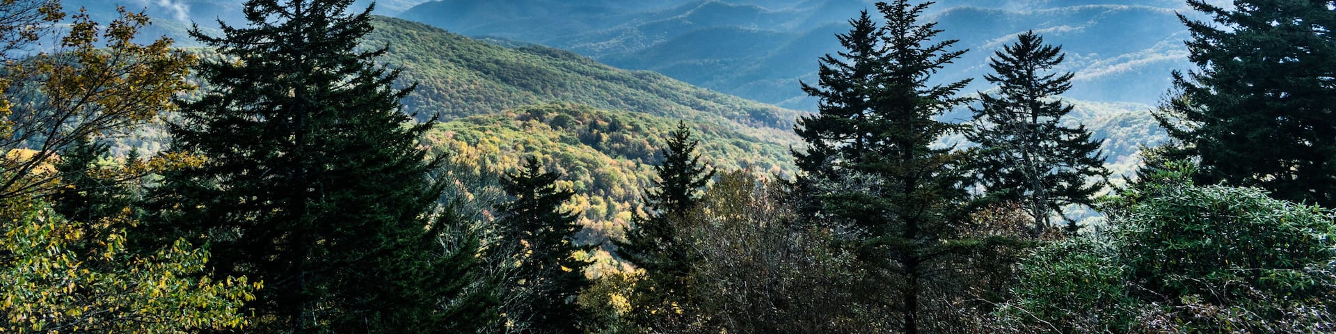 A mountain range with dense forests and a partly cloudy sky.