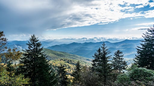 A mountain range with dense forests and a partly cloudy sky.