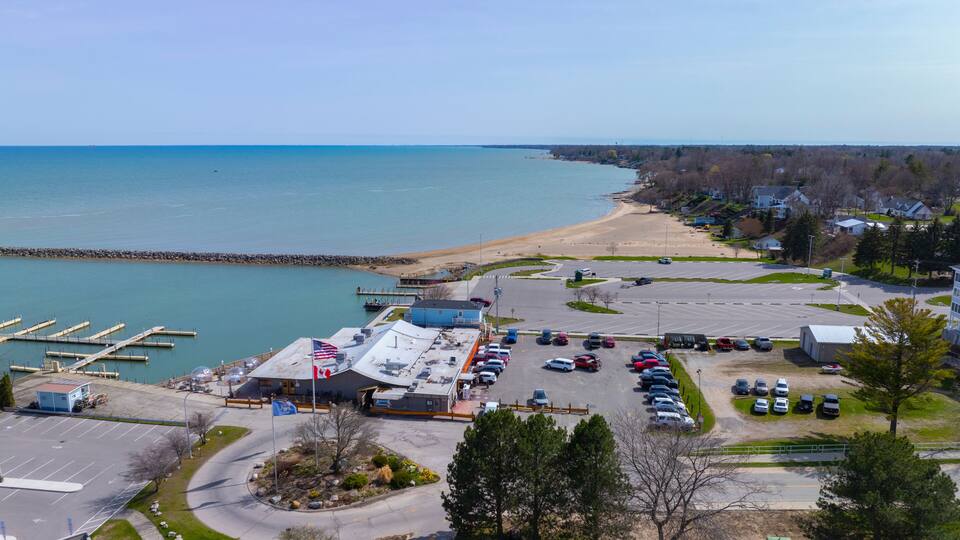 A coastal parking lot with a marina, a beach, and residential houses.