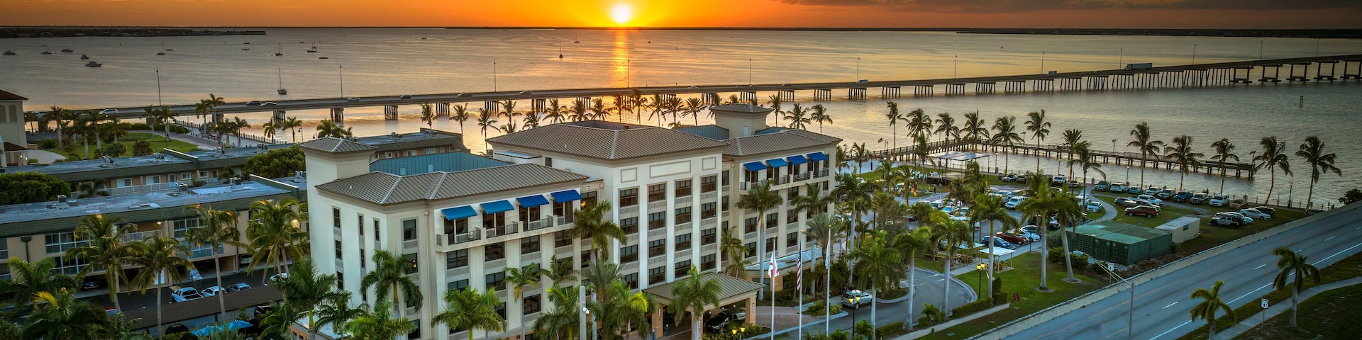 A coastal resort with a marina, palm trees, and a sunset.