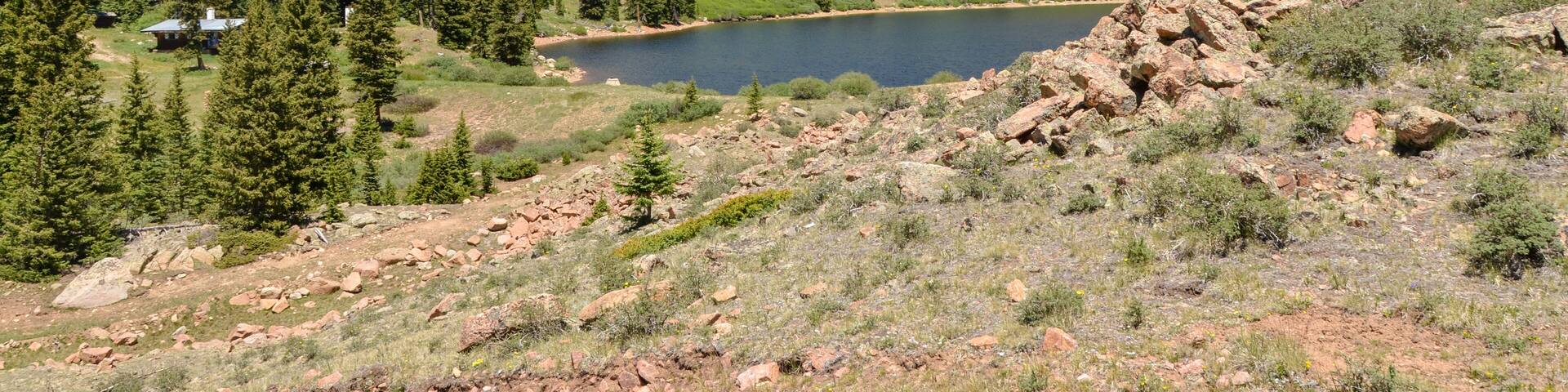 A mountainous landscape with a lake, forested areas, and a small cabin.