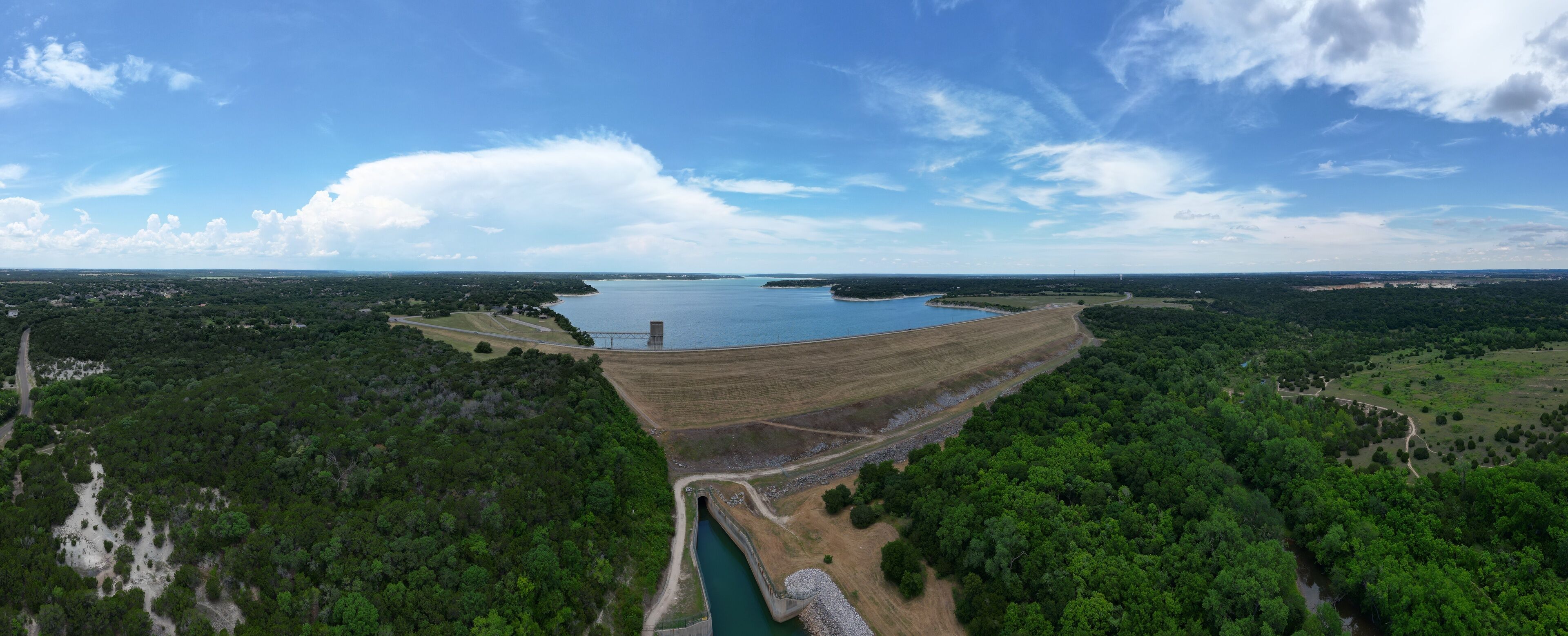 A large dam with a reservoir, surrounded by dense forest and open fields.
