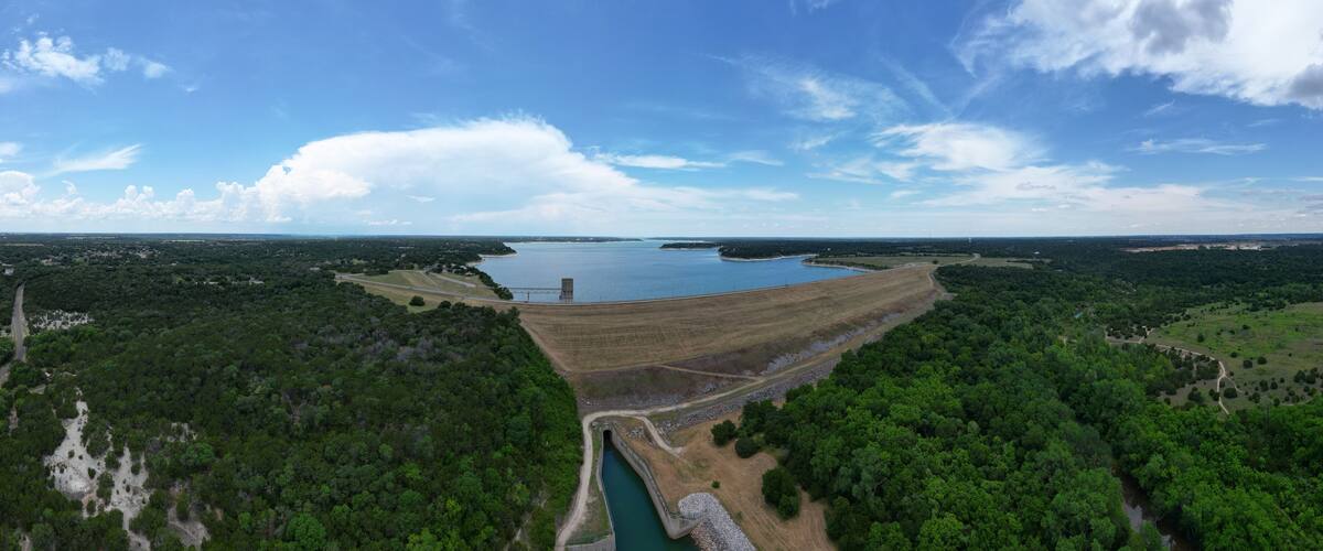 A large dam with a reservoir, surrounded by dense forest and open fields.