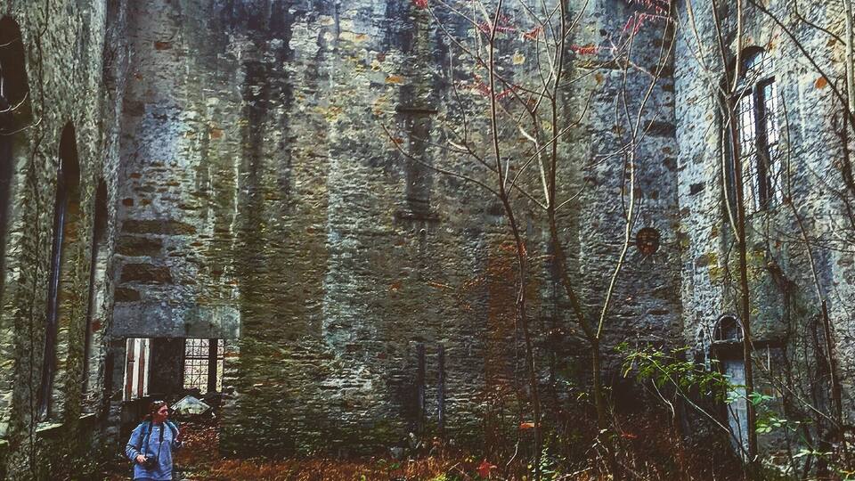 A dilapidated stone building with a collapsed roof and overgrown vegetation.