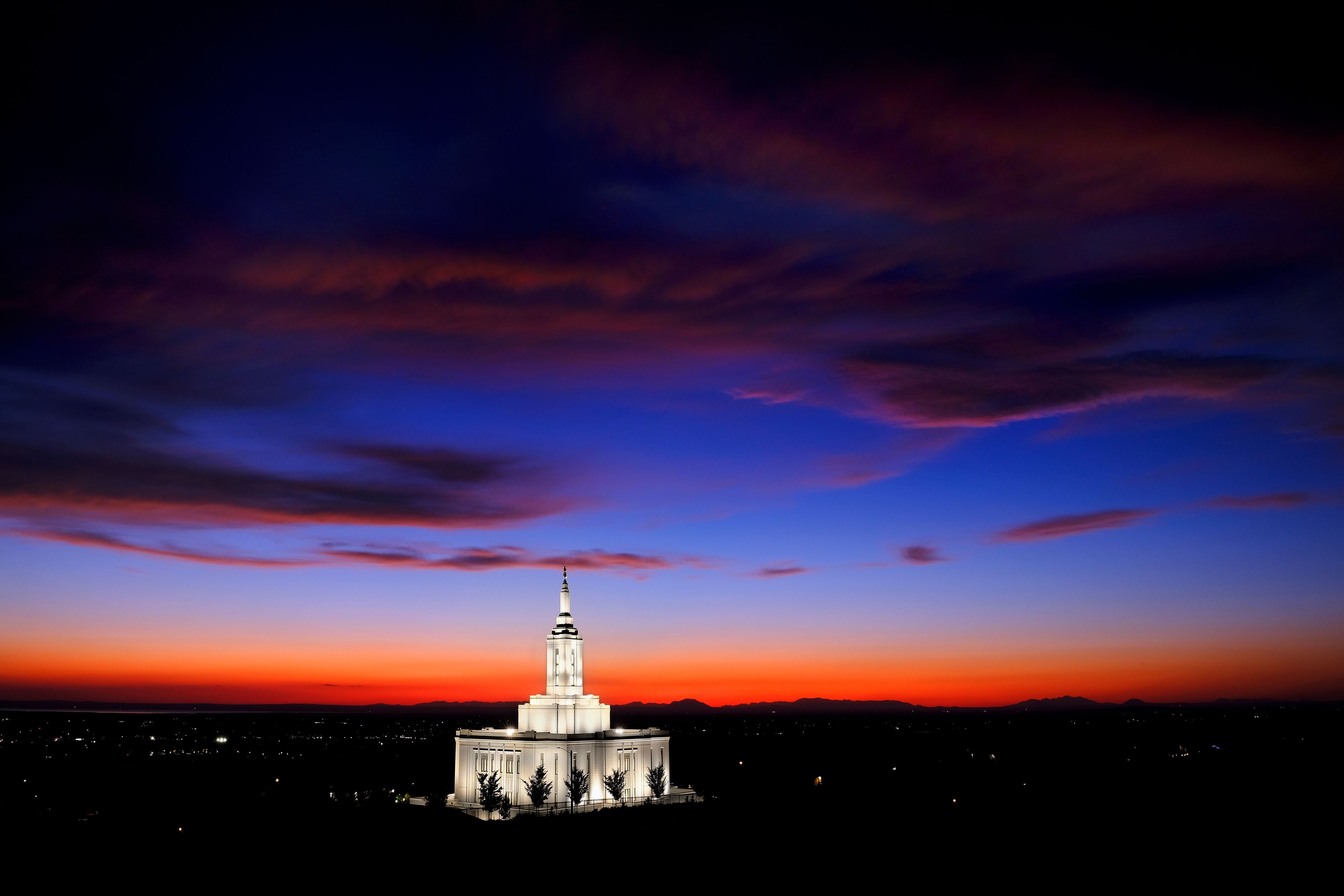 Um edifício grande e iluminado, com uma torre, sob um céu crepuscular com nuvens.