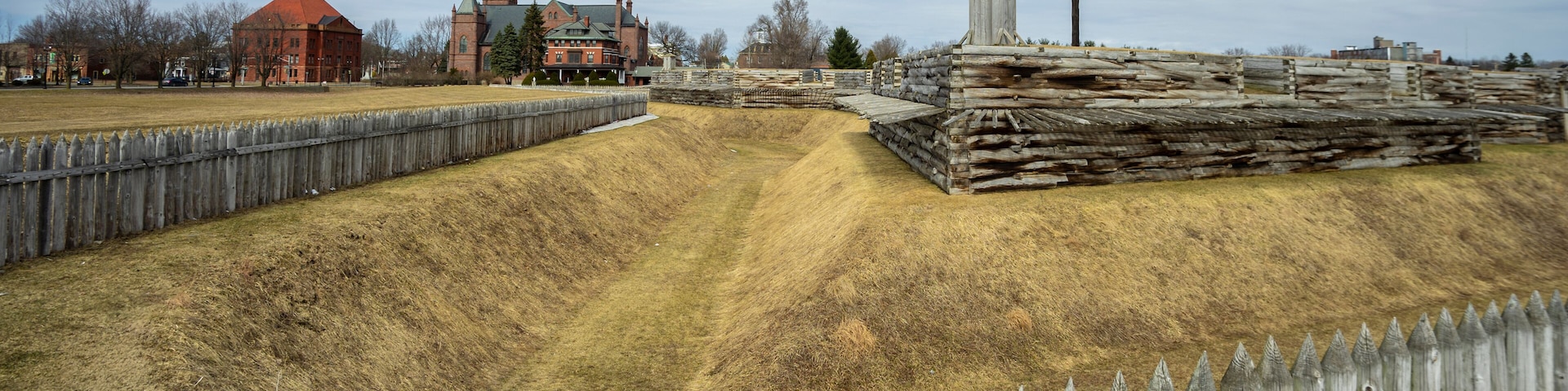 A historic fort with a wooden picket fence, a church, and a flagpole with an American flag.