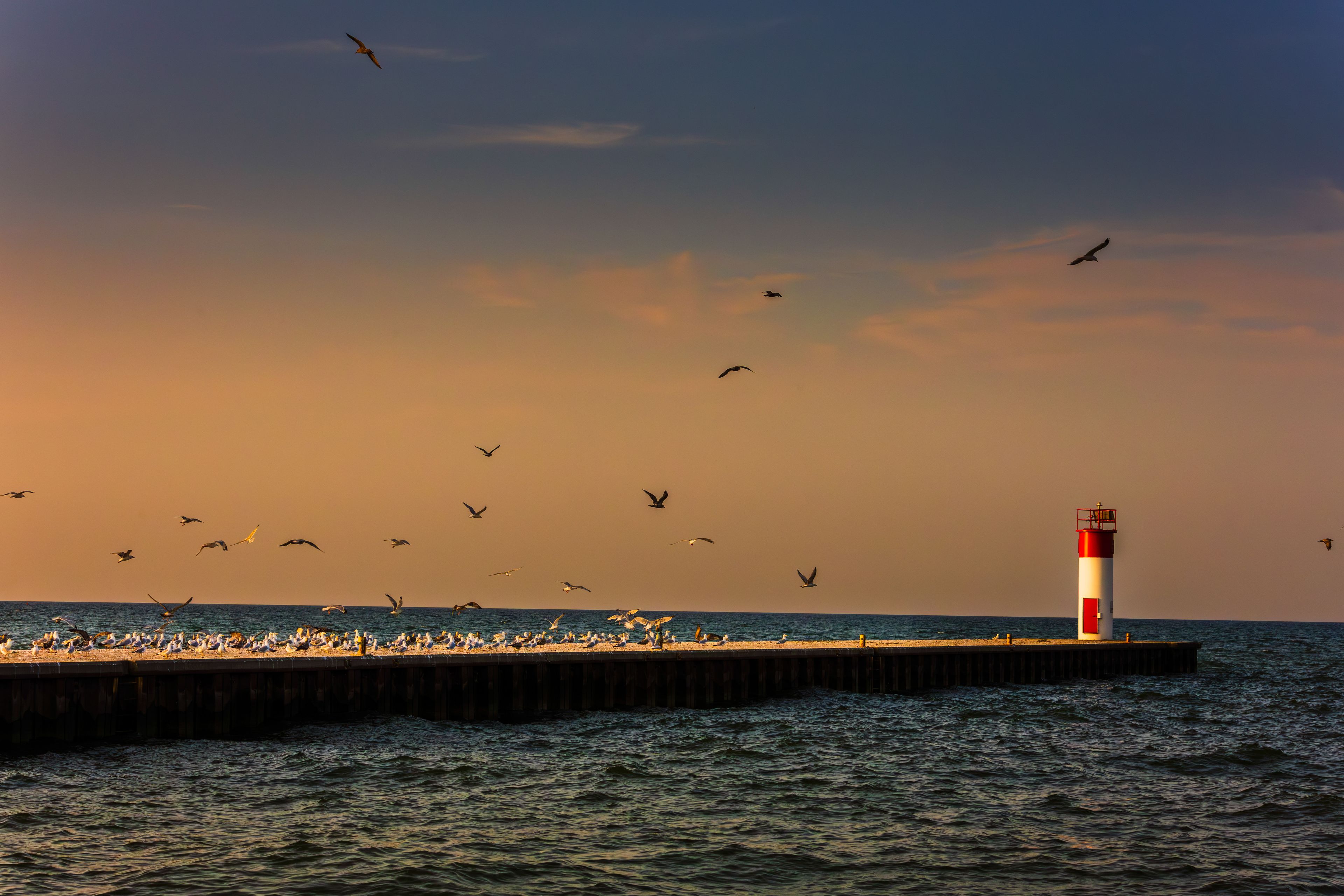 The historic white and red Port Dover West Pier Lighthouse stands as a sentinel on Lake Erie during a vibrant sunrise