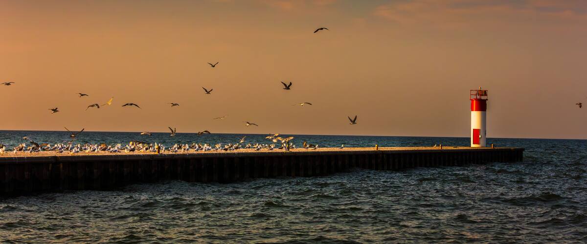 The historic white and red Port Dover West Pier Lighthouse stands as a sentinel on Lake Erie during a vibrant sunrise