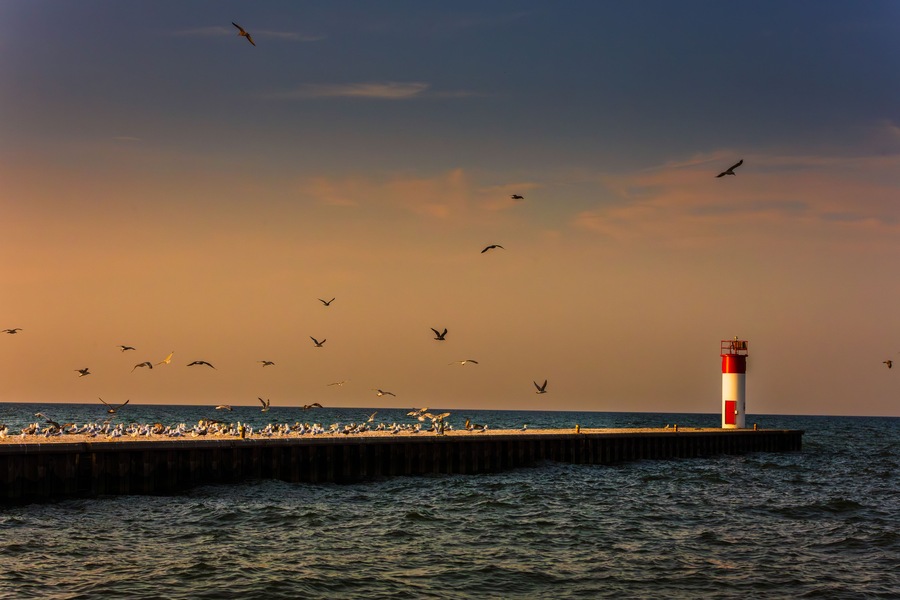 The historic white and red Port Dover West Pier Lighthouse stands as a sentinel on Lake Erie during a vibrant sunrise
