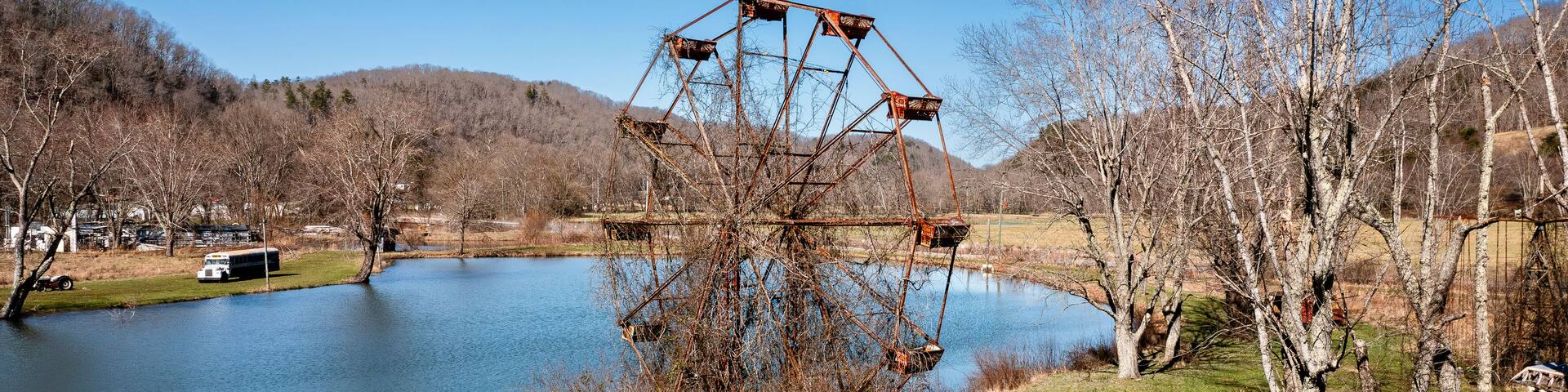 A rusted metal structure with a triangular frame and a circular platform, surrounded by trees and a body of water.