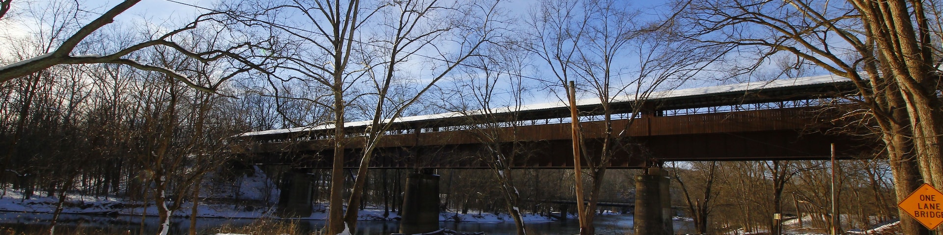 Eine schneebedeckte Straße unter einer Brücke, mit kahlen Bäumen und einem klaren Himmel.