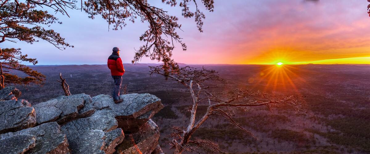 Man, person, standing on the edge of a cliff watching the sun setting on the horizon and a forest valley far below, Pulpit Rock, Cheaha State Park, Alabama