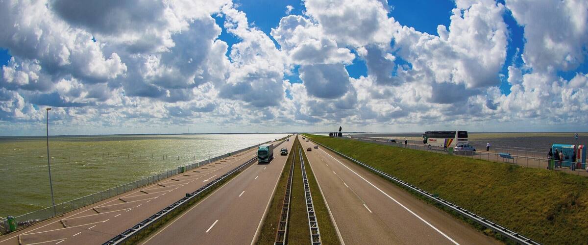 A highway with a clear sky and clouds, a bridge, and a body of water.