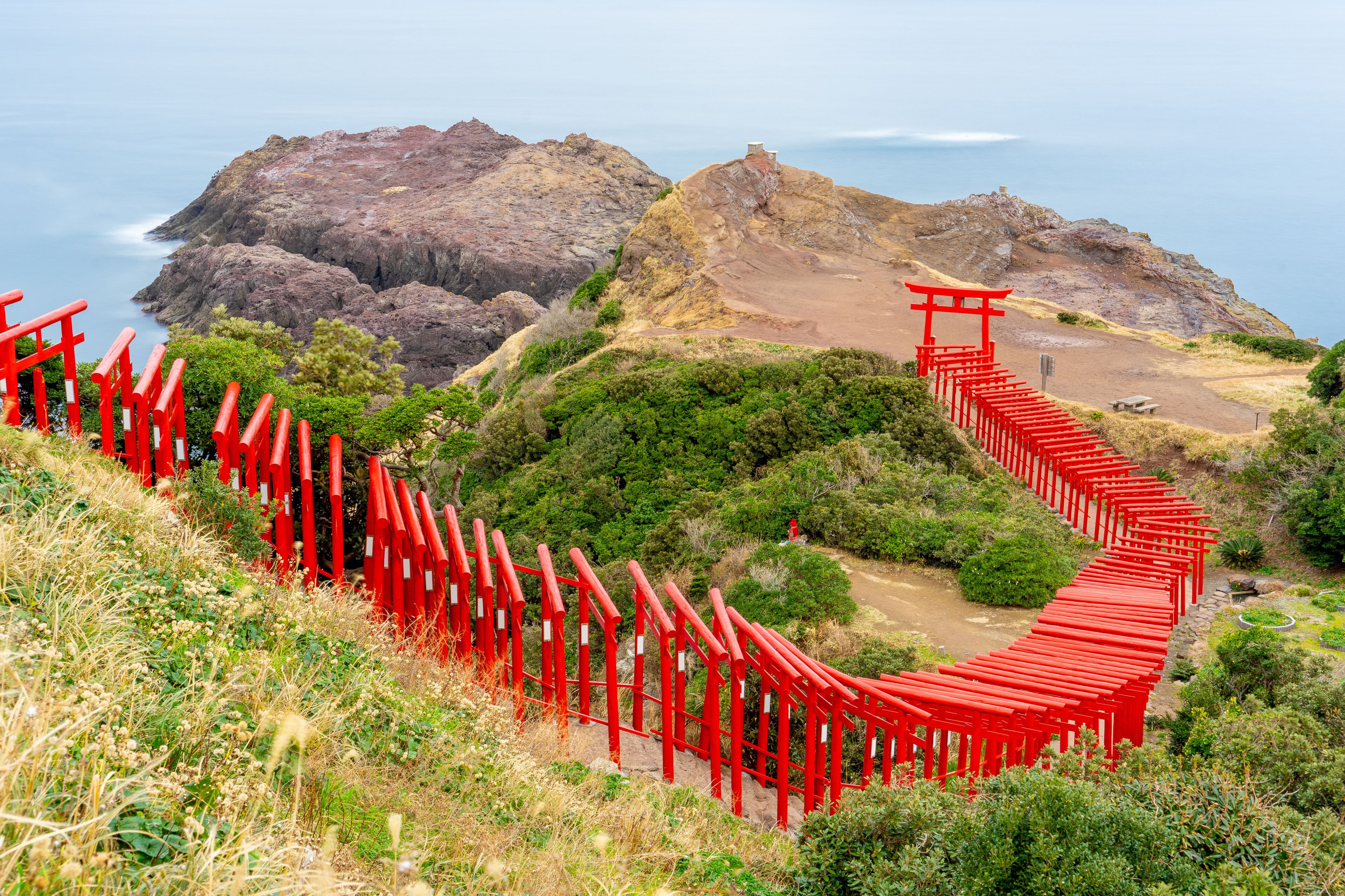 Motonosumi Inari Shrine with a long exposure in Yamaguchi Prefecture, Japan. 123 red torii gates aligned toward a seaside cliff overlooking the Japan Sea.
