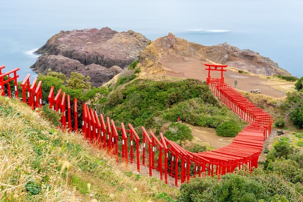 Motonosumi Inari Shrine with a long exposure in Yamaguchi Prefecture, Japan. 123 red torii gates aligned toward a seaside cliff overlooking the Japan Sea.