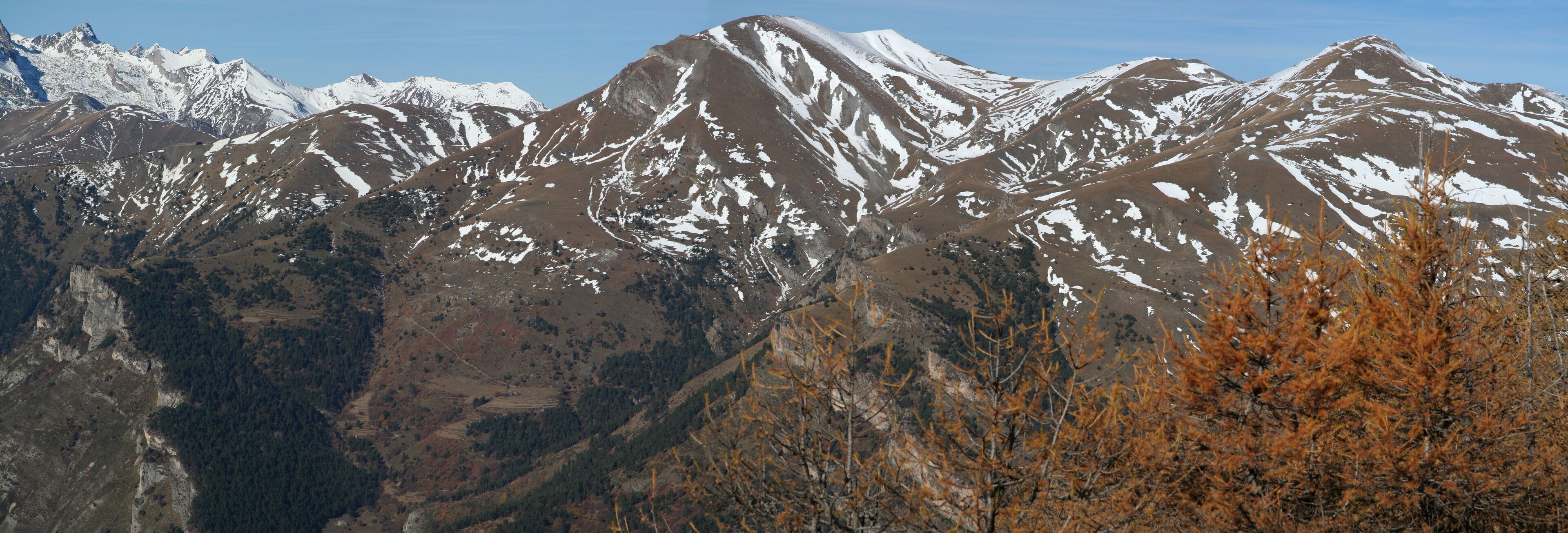 Snow-capped mountains, a valley, and autumn-colored trees.