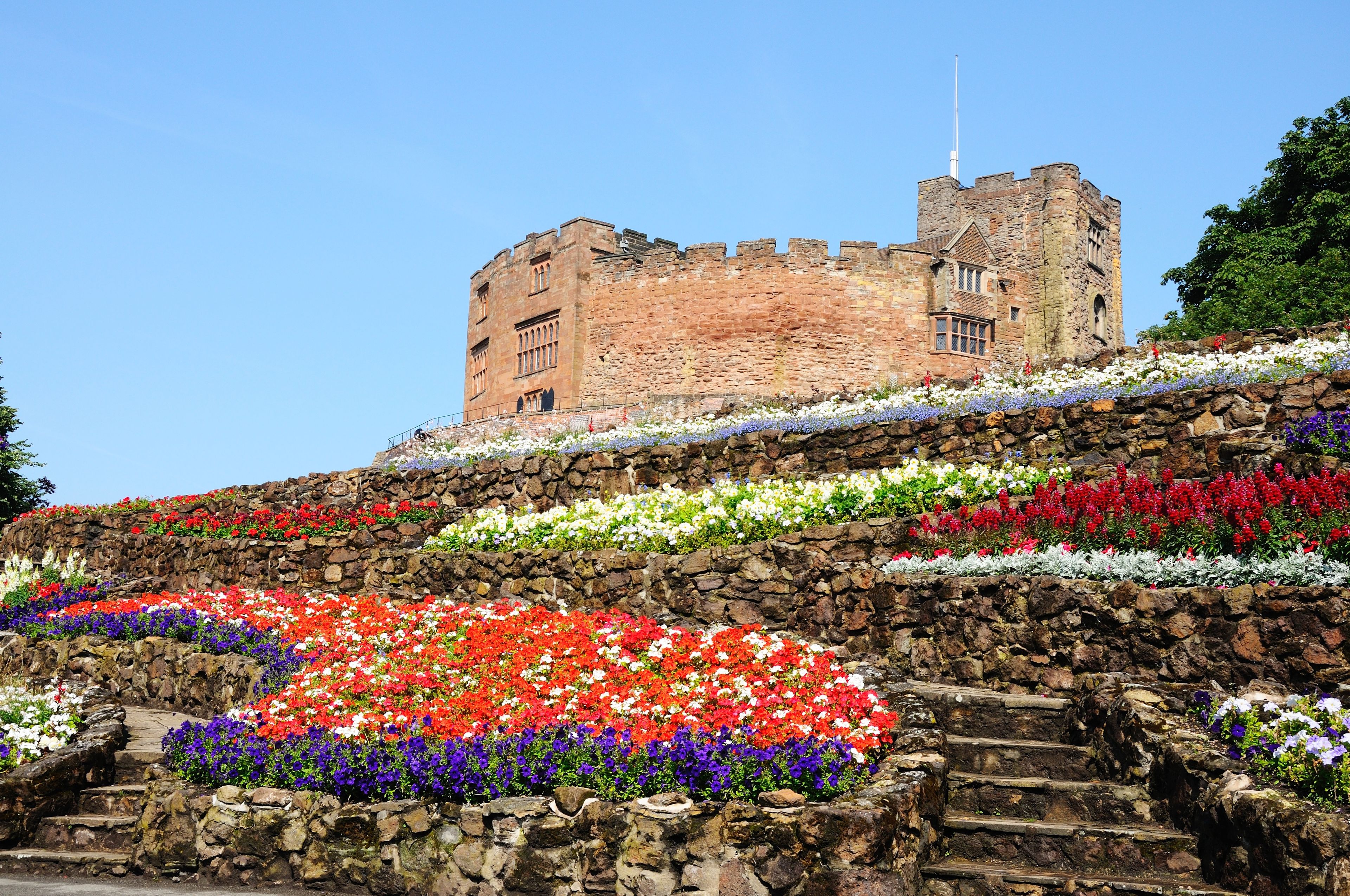 A historic castle with a stone wall adorned with colorful flower beds.