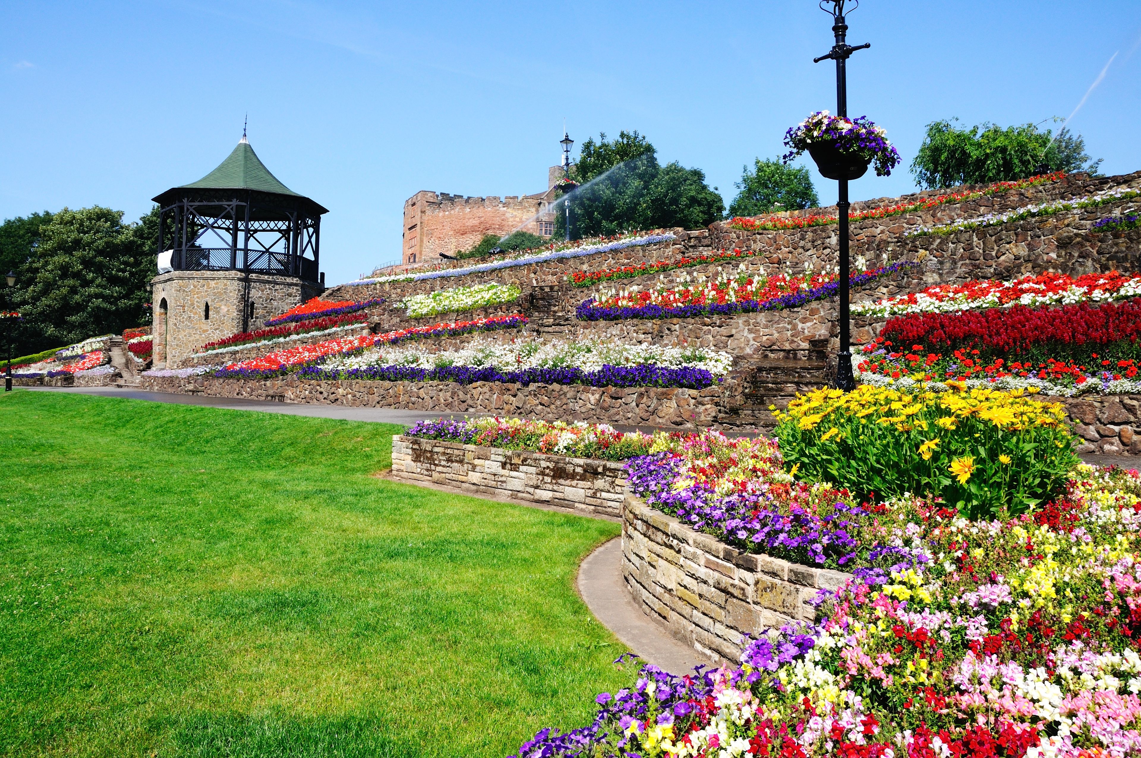 A garden with a stone wall, a gazebo, and a variety of colorful flowers.