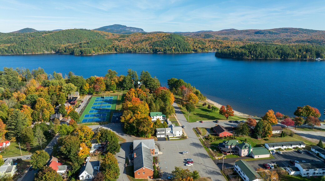 Aerial view of Schroon Lake, New York, showcasing the calm lake, fall foliage, and small town structures nestled along the shoreline under a clear sky.