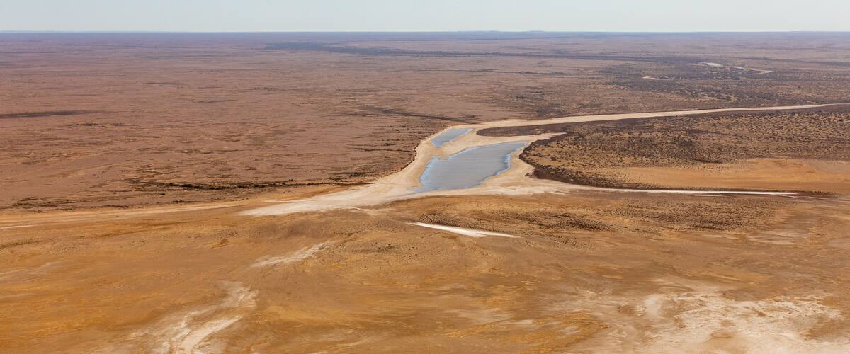 A vast arid landscape with a winding river and a dirt road.